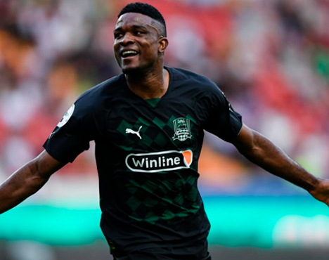 Вижу футболиста в чёрной форме на фоне стадиона, он празднует гол с разведенными руками. На форме заметны логотипы Puma и Winline